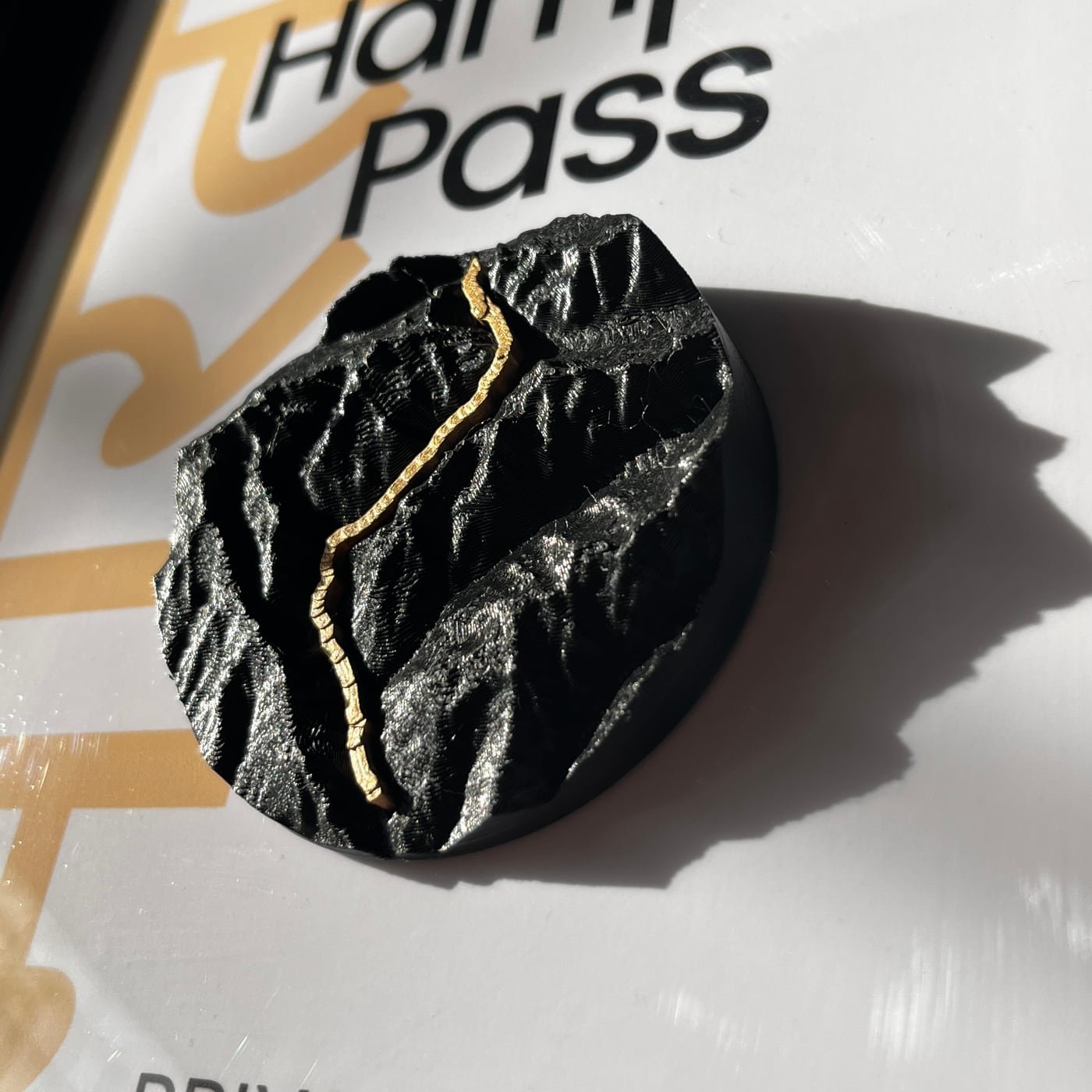 Close view of the printed charcoal terrain standing proud of the poster, a gold-coloured trail running across it